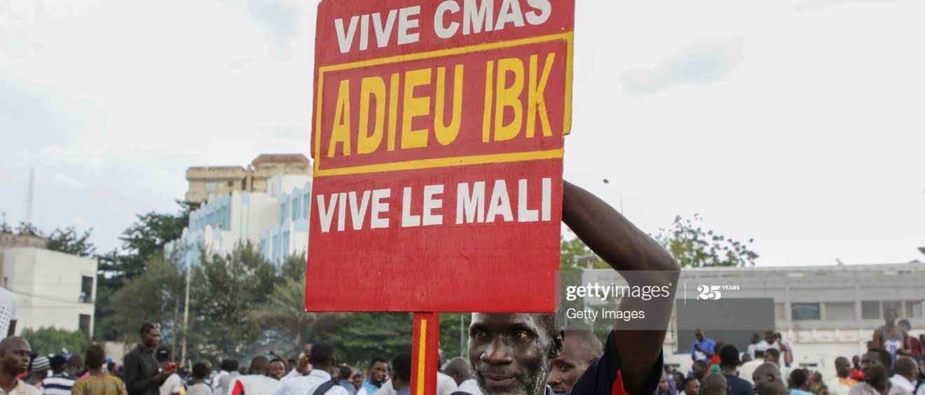 18 août 2020, homme malien tenant une pancarte en faveur d'une démission d'Ibrahim Boubacar Keita. Dans un même temps, les militaires paradent sur le Boulevard de l'Indépendance, après l'arrestation d'Ibrahim Boubacar Keita.